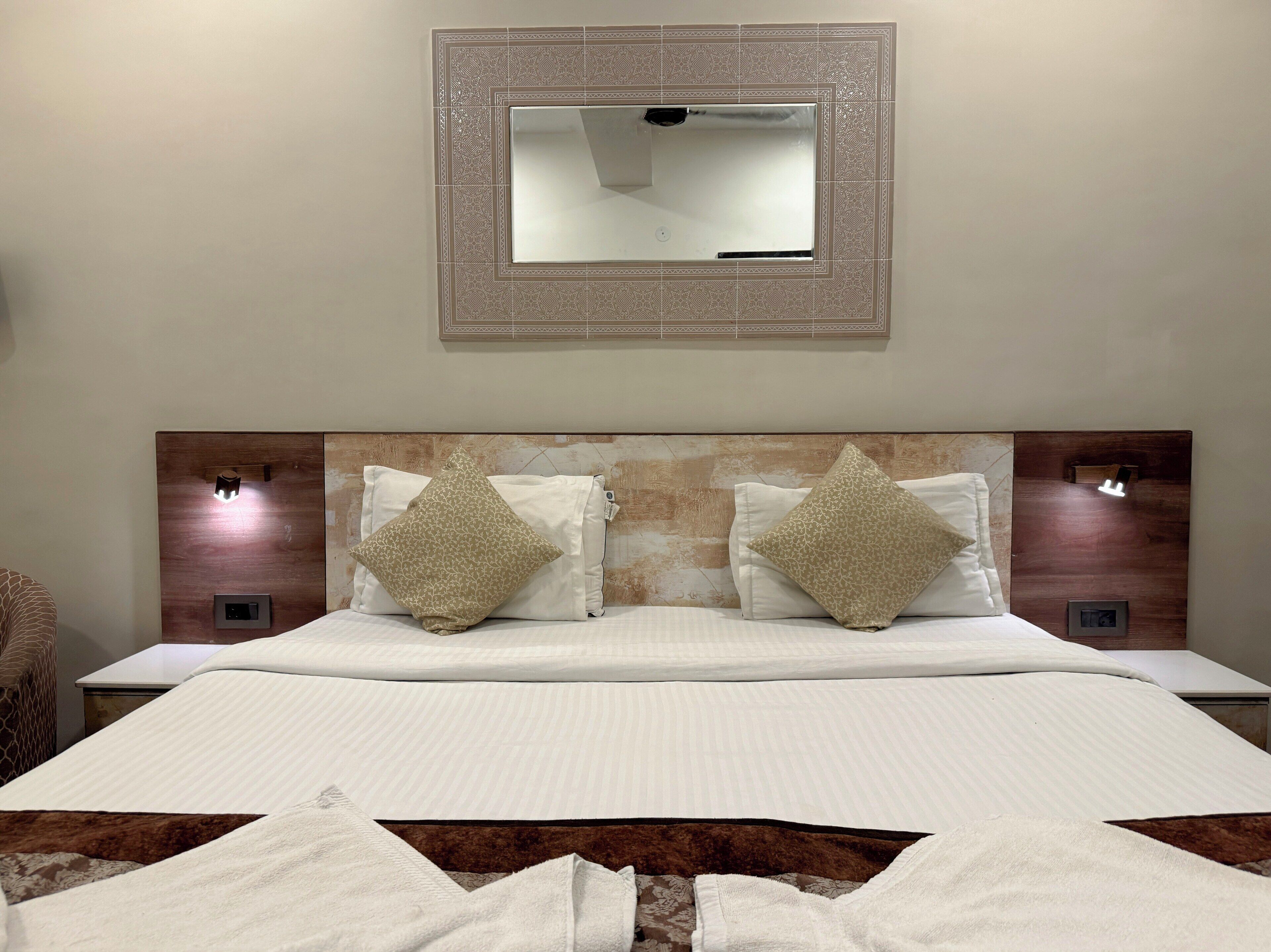 A neatly made bed with two pillows, a headboard with a built-in light, and a wall-mounted mirror.