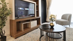 Un soggiorno moderno con una televisione a schermo piatto montata su una parete attrezzata in legno, un tavolino rotondo, una poltrona grigia e una pianta in vaso.