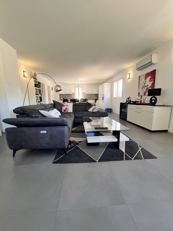 A modern living room with a sectional sofa, a coffee table, and a kitchen in the background. - Apartment T4 “Notta Bene”, between sea and mountains (Porto-Vecchio)