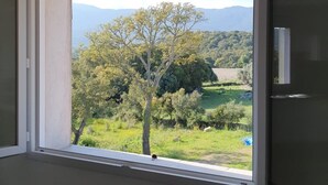 Una habitación con un ventanal que ofrece vistas a un árbol y un paisaje montañoso.