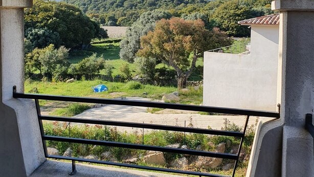 Un balcón con vista a un paisaje montañoso, cielo despejado y un edificio distante.