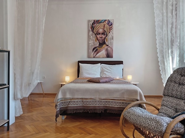 A bedroom with a bed, two bedside lamps, a chair, and a painting on the wall.