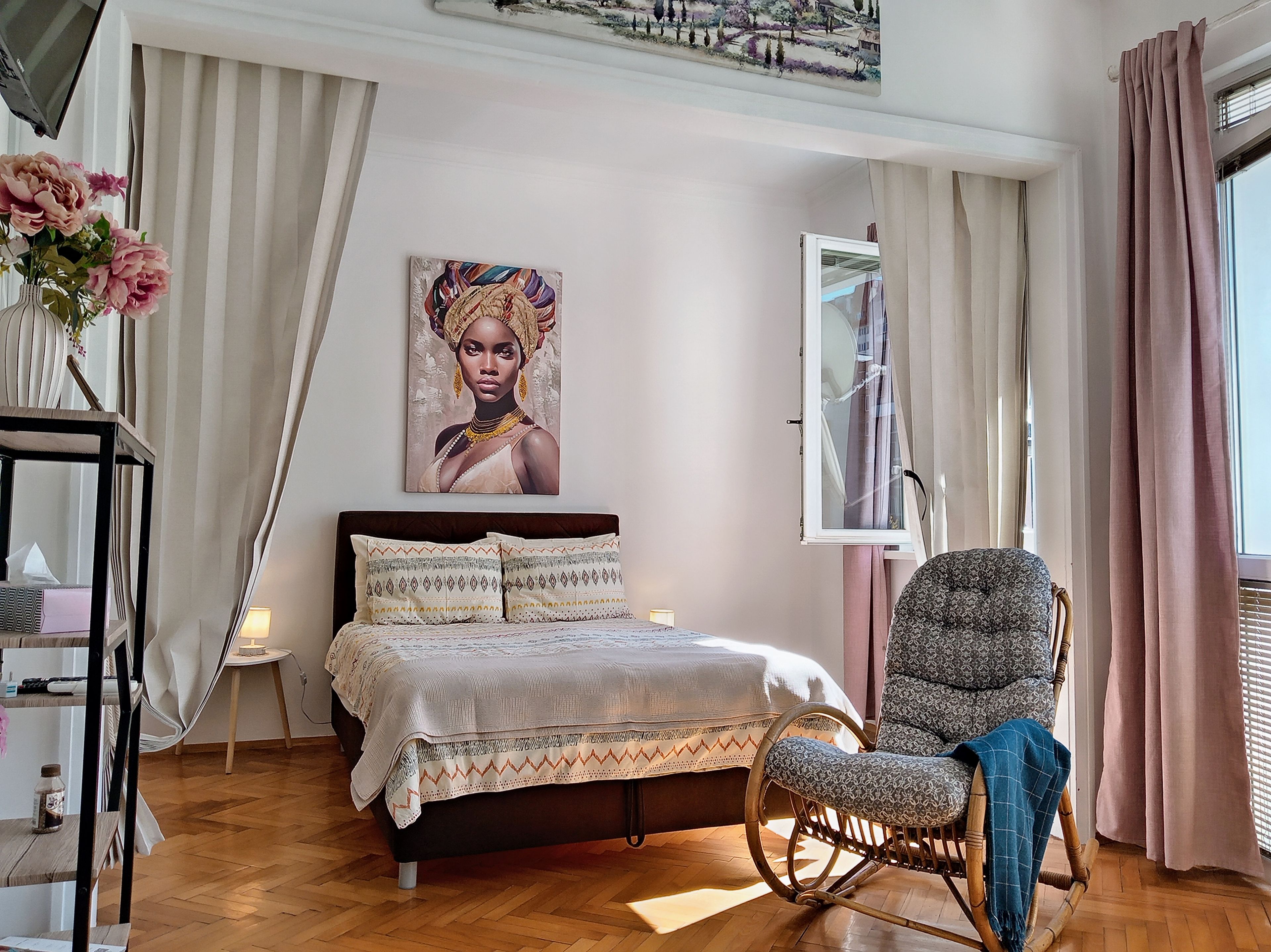A bedroom with a bed, a chair, a painting, and a window with curtains.