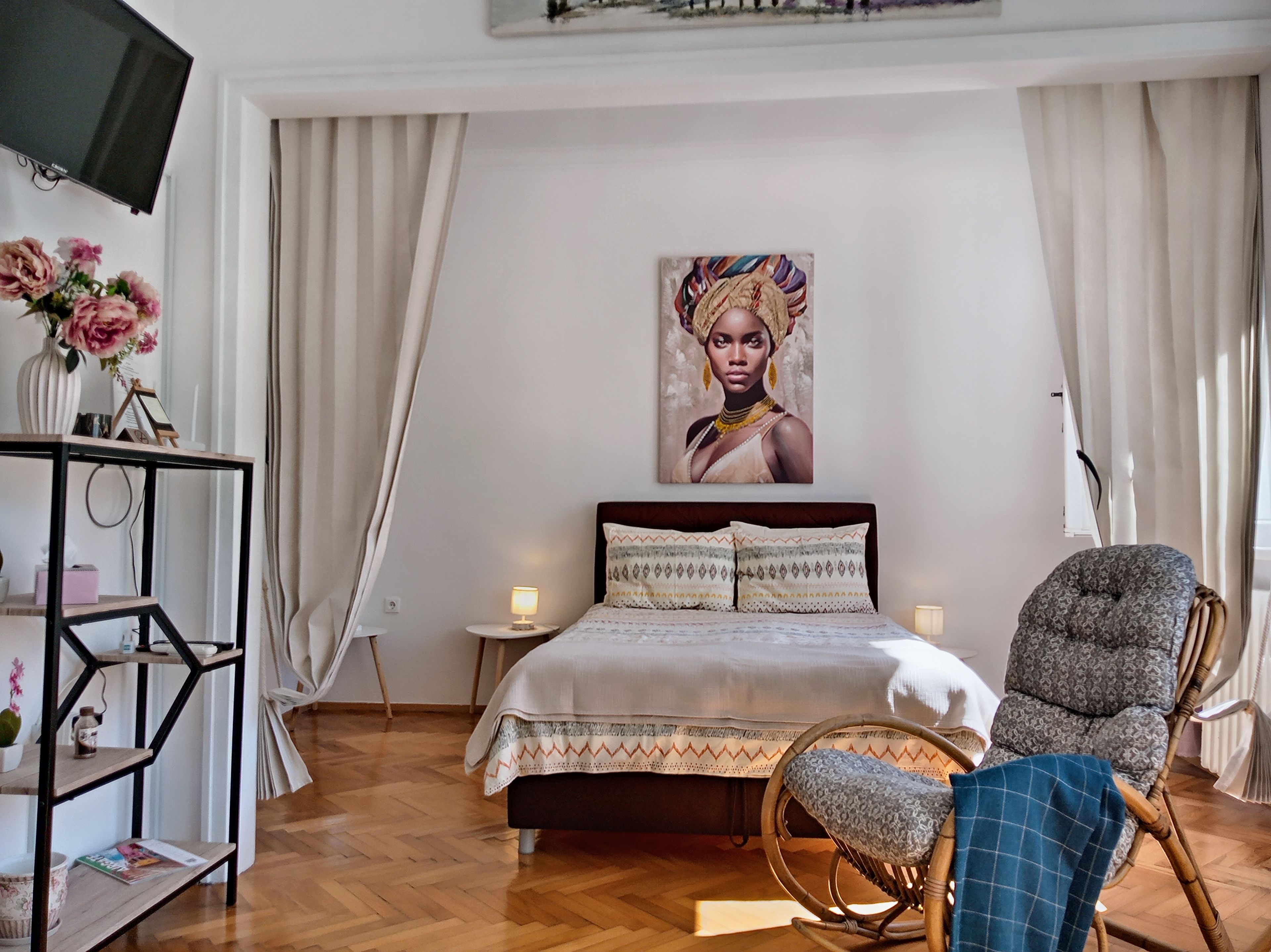 Une chambre à coucher avec un lit, une chaise, un téléviseur, un tableau et un bureau agrémenté d’un vase de fleurs.