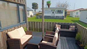 Une terrasse dotée de meubles en osier, d’une porte vitrée et offrant une vue sur un quartier résidentiel.