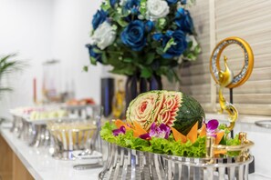 A buffet table with a watermelon centerpiece, surrounded by various dishes and a decorative mirror. - Thai Ha Boutique Hotel (Bai Chay)