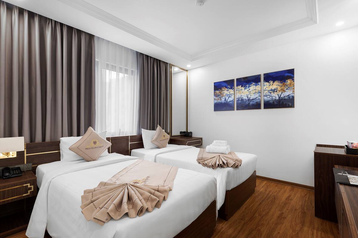A hotel room with two beds, a desk, a telephone, and artwork on the wall.