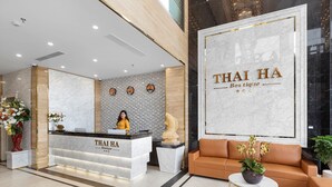 A reception area with a marble counter labeled "THAI HA Boutique," a receptionist, and a sofa with a potted plant. - Thai Ha Boutique Hotel (Bai Chay)