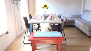 A dining area with a table, chairs, a bench, a TV mounted on the wall, a framed picture, and a sunflower on the table.