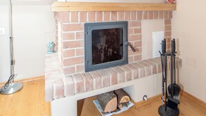 A room with a brick fireplace, a wooden mantel, and a window with a view of trees.