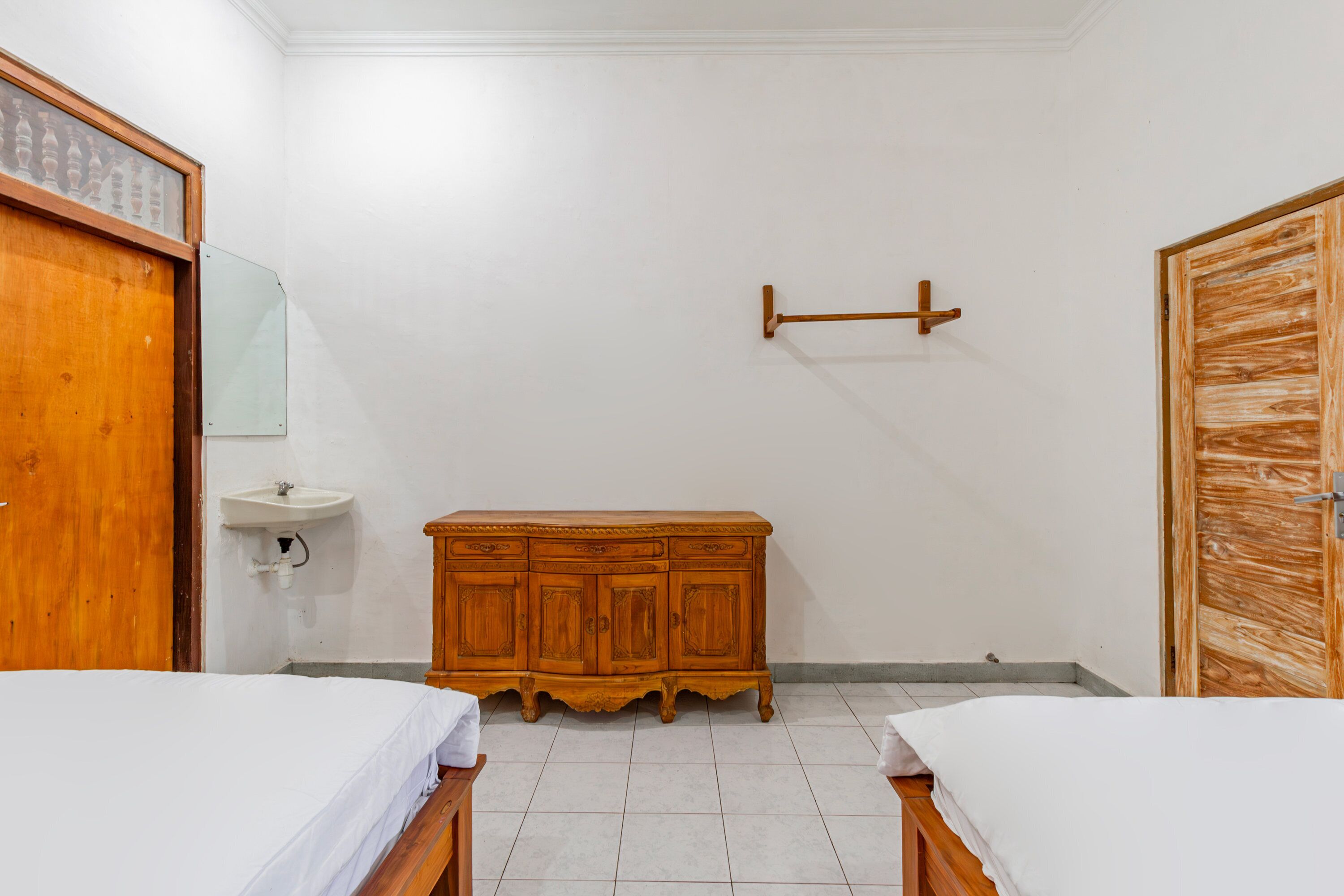 A bedroom with two beds, a wooden dresser, a mirror, and a wooden door.