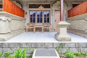 Un bâtiment traditionnel doté d’un porche carrelé, de deux chaises en bois, d’une petite table et d’un pilier en pierre servant d’élément décoratif.