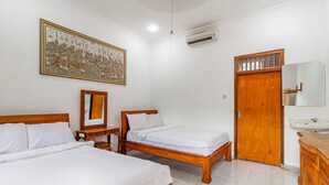 A hotel room with two wooden beds, a large decorative wall hanging, a wooden wardrobe, a mirror, and a bathroom with a sink. - Belvilla Ratna Resort Ubud PalaceNearUbud Palace (Ubud)