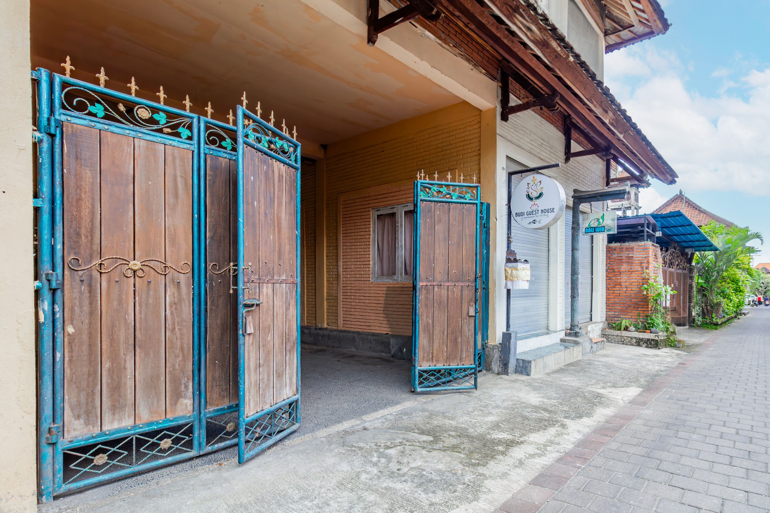 A traditional wooden gate with decorative metalwork, leading to a building with a brick facade and a sign indicating a guest house.