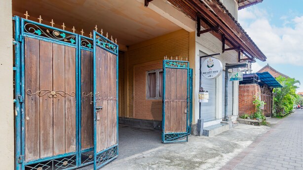 A traditional wooden gate with decorative metalwork, leading to a building with a brick facade and a sign indicating a guest house. - Belvilla Ratna Resort Ubud PalaceNearUbud Palace (Ubud)