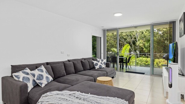 A modern living room with a grey sectional sofa, a flat-screen TV, and a balcony with a view of greenery. - Sounds of the Ocean on Boyd (WOORIM)
