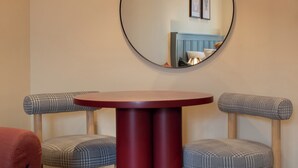 Un comedor con una mesa redonda, dos sillas, un pilar rojo, una lámpara colgante y un espejo redondo en la pared.