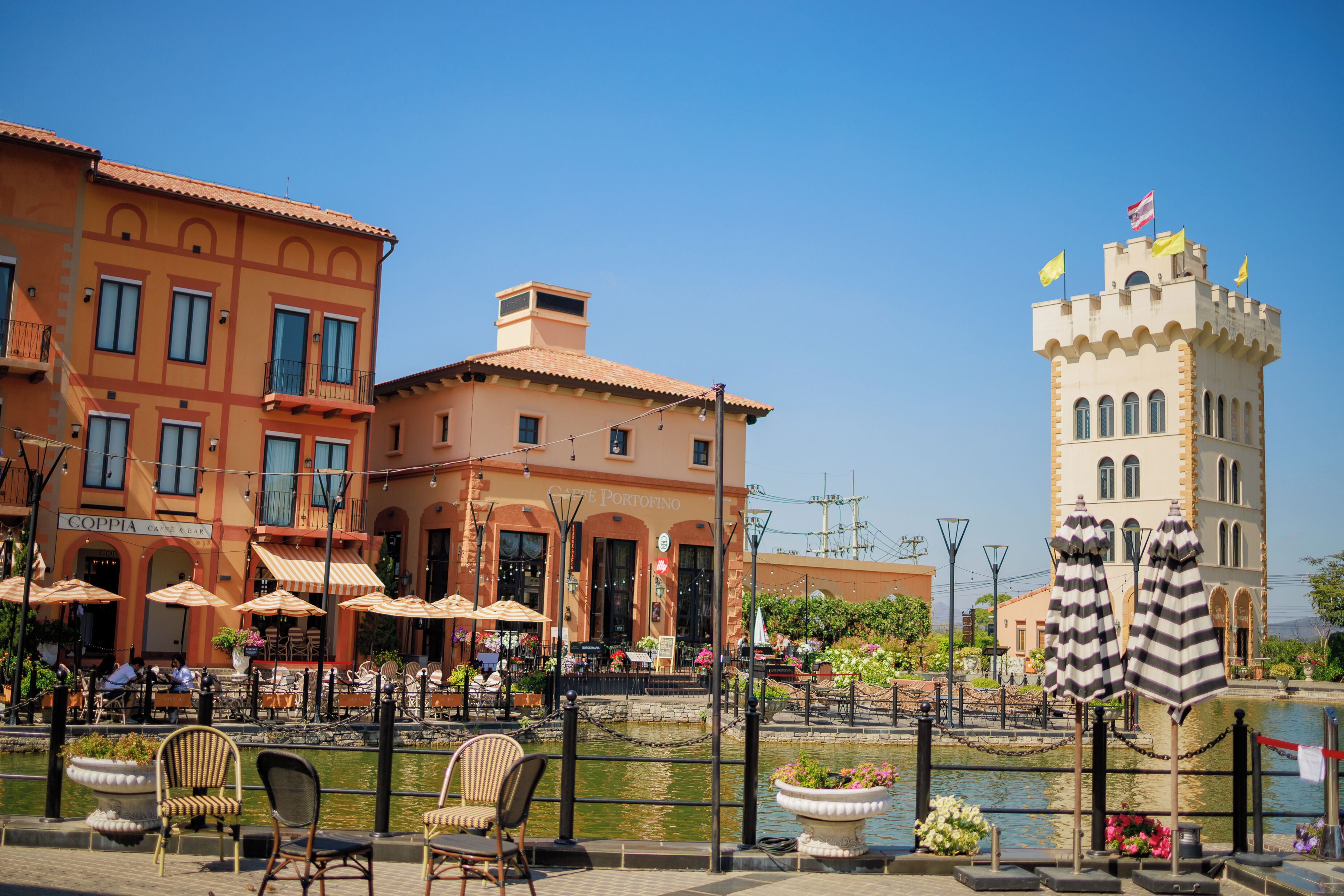 A waterfront restaurant with outdoor seating, a canal, and a castle-like building in the background.