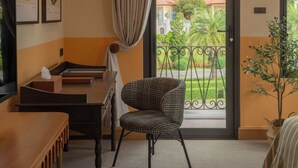 Habitación de hotel con balcón, escritorio, silla y dos cuadros en la pared.