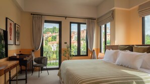Habitación de hotel con una cama grande, un escritorio, una silla y vistas a edificios a través de las ventanas.