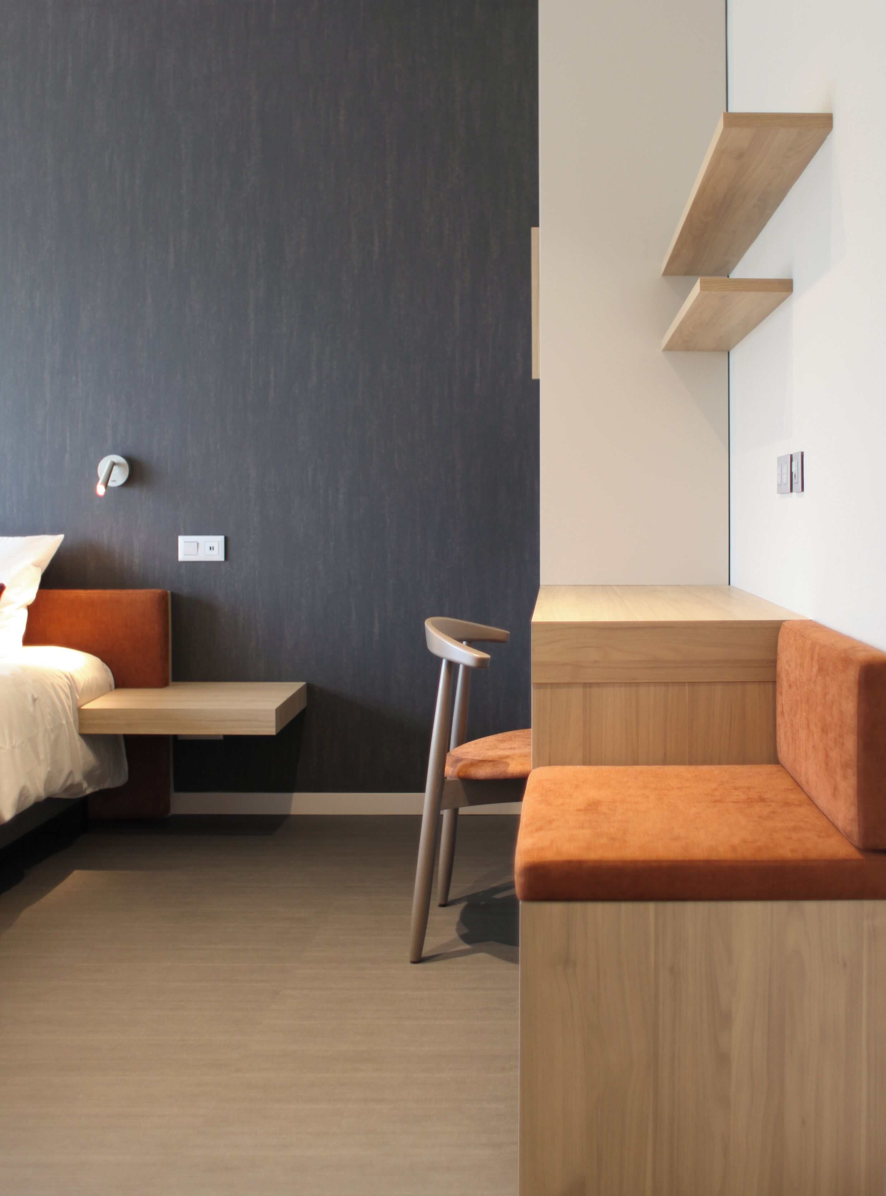 Quarto moderno com cama, um banco, um banquinho e uma estante embutida.