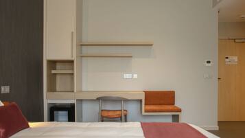 A modern hotel room with a bed, a desk, a chair, and a small table with a cushion.