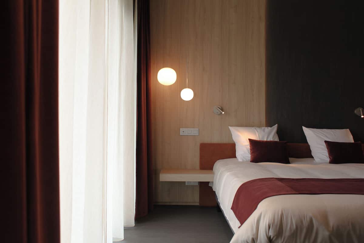Quarto de hotel com uma cama, mesa de cabeceira e luminária fixada na parede.