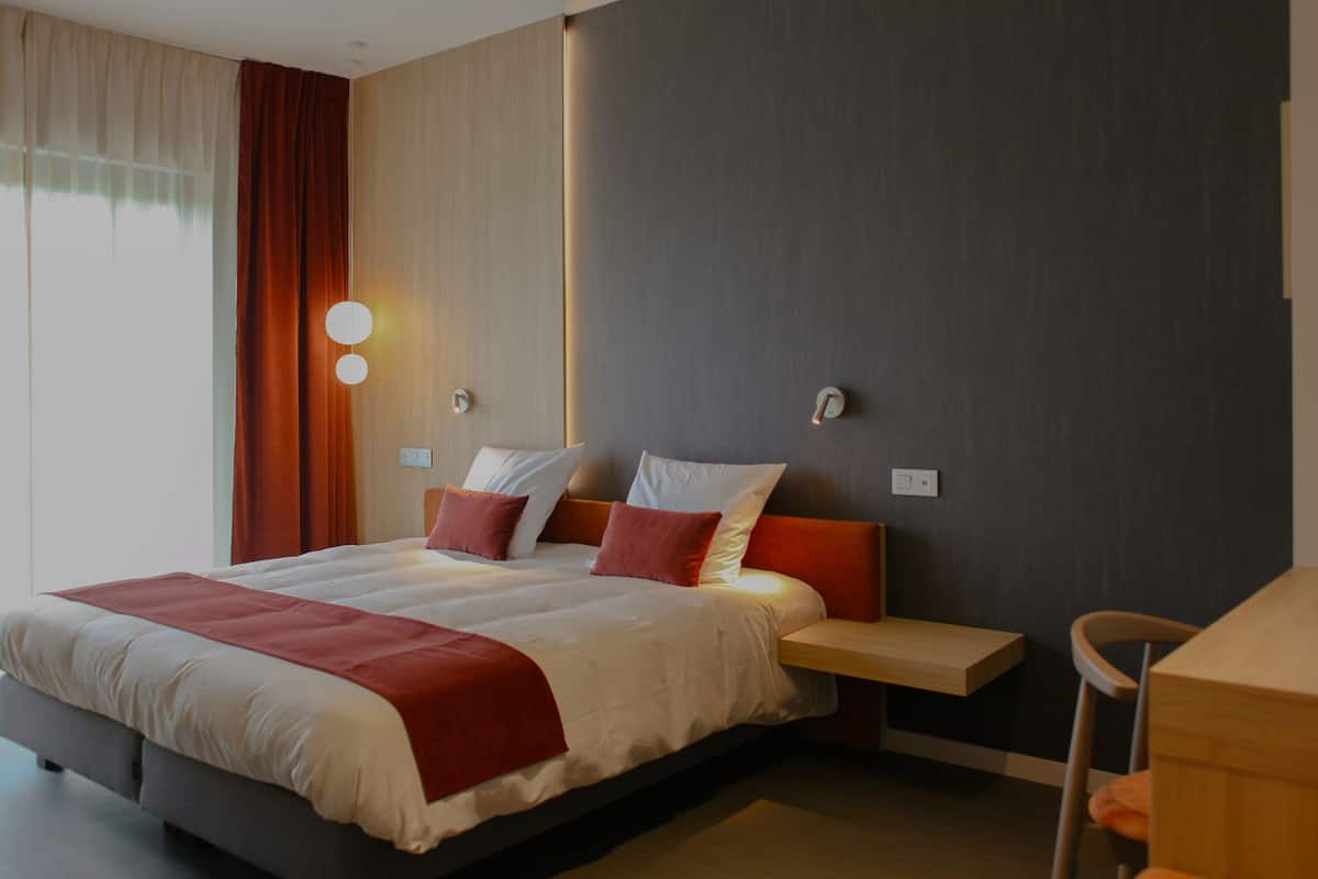 Quarto de hotel moderno com uma cama grande, mesas de cabeceira e uma escrivaninha.