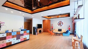 A spacious living area with a wooden floor, a sofa, a coffee table, and a TV. There is a colorful cabinet with drawers and a small fireplace. - Sun lake Hotel (Yuchi)