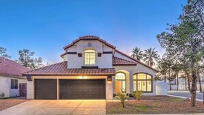 A two-story house with a garage, a tiled roof, and a small front yard with landscaping. - Entertainment Galore in 4BR Oasis w/ Pool! (North Las Vegas)