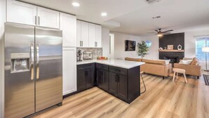 A modern kitchen with dark cabinets, a stainless steel refrigerator, and a white countertop. - Entertainment Galore in 4BR Oasis w/ Pool! (North Las Vegas)