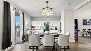 Une cuisine moderne avec des meubles blancs, un lustre et un coin repas comprenant quatre chaises.
