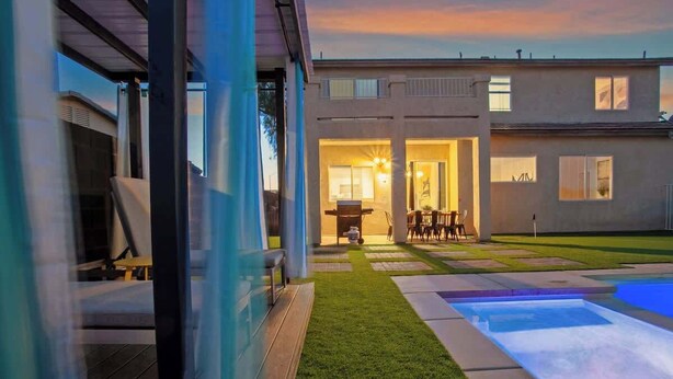 Une maison moderne dotée d’une pelouse bien entretenue, d’une piscine et d’un espace patio aménagé avec du mobilier d’extérieur.