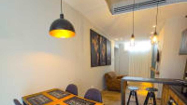 A dining area with a wooden table and chairs, a kitchen with a counter and stools, and pendant lighting.