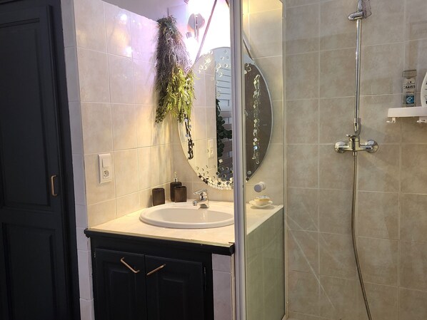 A bathroom with a white sink, dark cabinets, a mirror with a decorative frame, and a shower area. - la Maison Bleu Avec Spa (Fayence)
