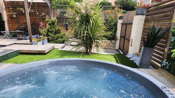 A hot tub in a backyard with a wooden deck, a small garden, and a stone wall.