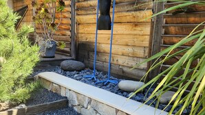 A wooden cabin with a garden area featuring a stone pathway, potted plants, and a blue sculpture.