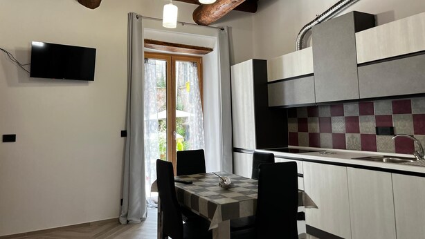 A modern kitchen with a built-in stove, a dining area with a table and chairs, and a TV mounted on the wall. - Z-y-x- Residence Archive 180 (Cesinali)