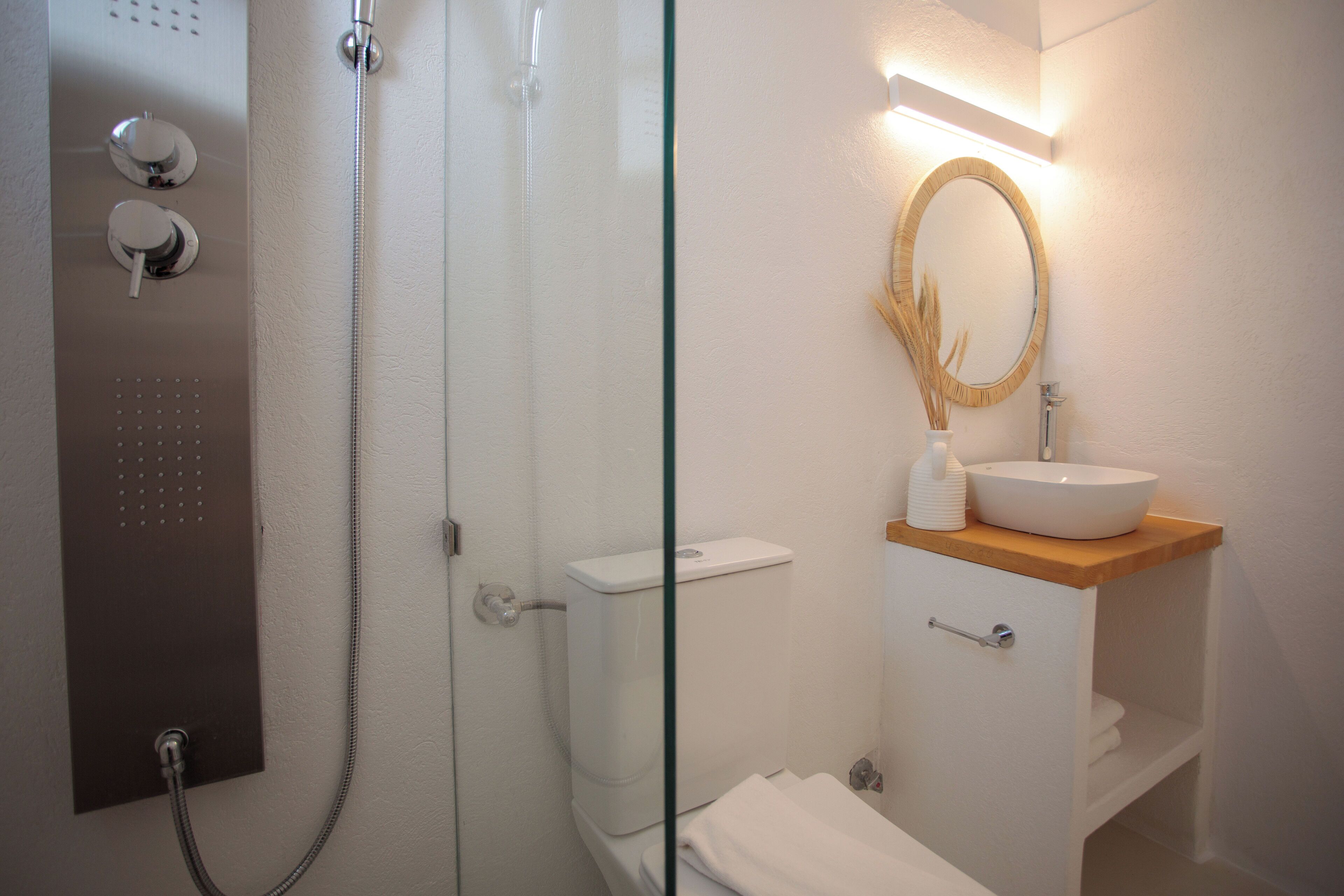 A bathroom with a glass-enclosed shower, a white toilet, and a wooden vanity with a white sink and mirror.