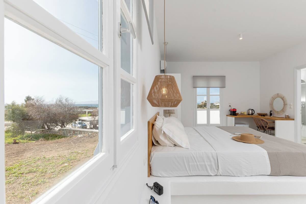 A bedroom with a large window, a bed, a desk, and a hanging light fixture.