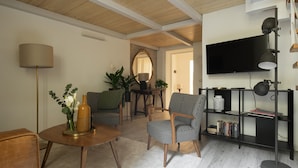 Una sala de estar moderna con una mesa redonda de madera, dos sillones estampados, una lámpara de pie, una estantería y un televisor de pantalla plana.