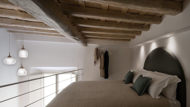 Un dormitorio con una cama grande, un balcón con barandilla y vigas de madera en el techo.