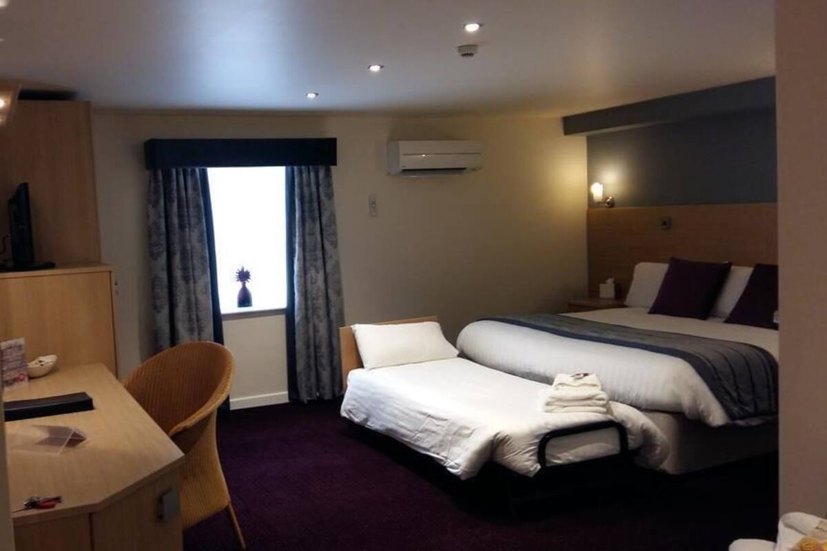 Ein Hotelzimmer mit Bett, Schreibtisch, Stuhl und einem Fenster mit Vorhängen.
