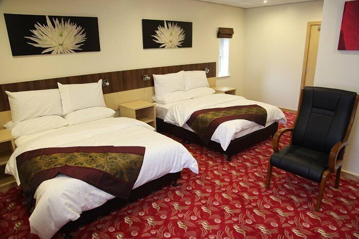 Ein Hotelzimmer mit zwei Betten, einem roten Teppich mit Muster und einem schwarzen Ledersessel.