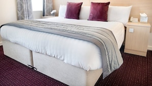 A hotel room with a large bed, a nightstand, a lamp, and a window with curtains. - Cambridge Hotel Waterfront (Brighouse)