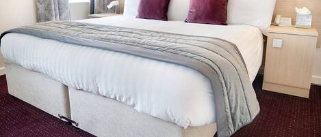 Une chambre d’hôtel avec un grand lit, une table de chevet, une lampe et une fenêtre avec des rideaux.