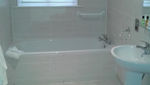 A bathroom with a bathtub, a sink, and a window with blinds. - Cambridge Hotel Waterfront (Brighouse)