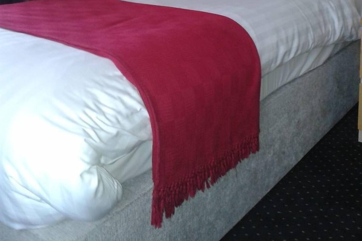 Ein Hotelzimmer mit einem Bett, einer roten Tagesdecke, weißen Kissen und einem Holzkopfende.