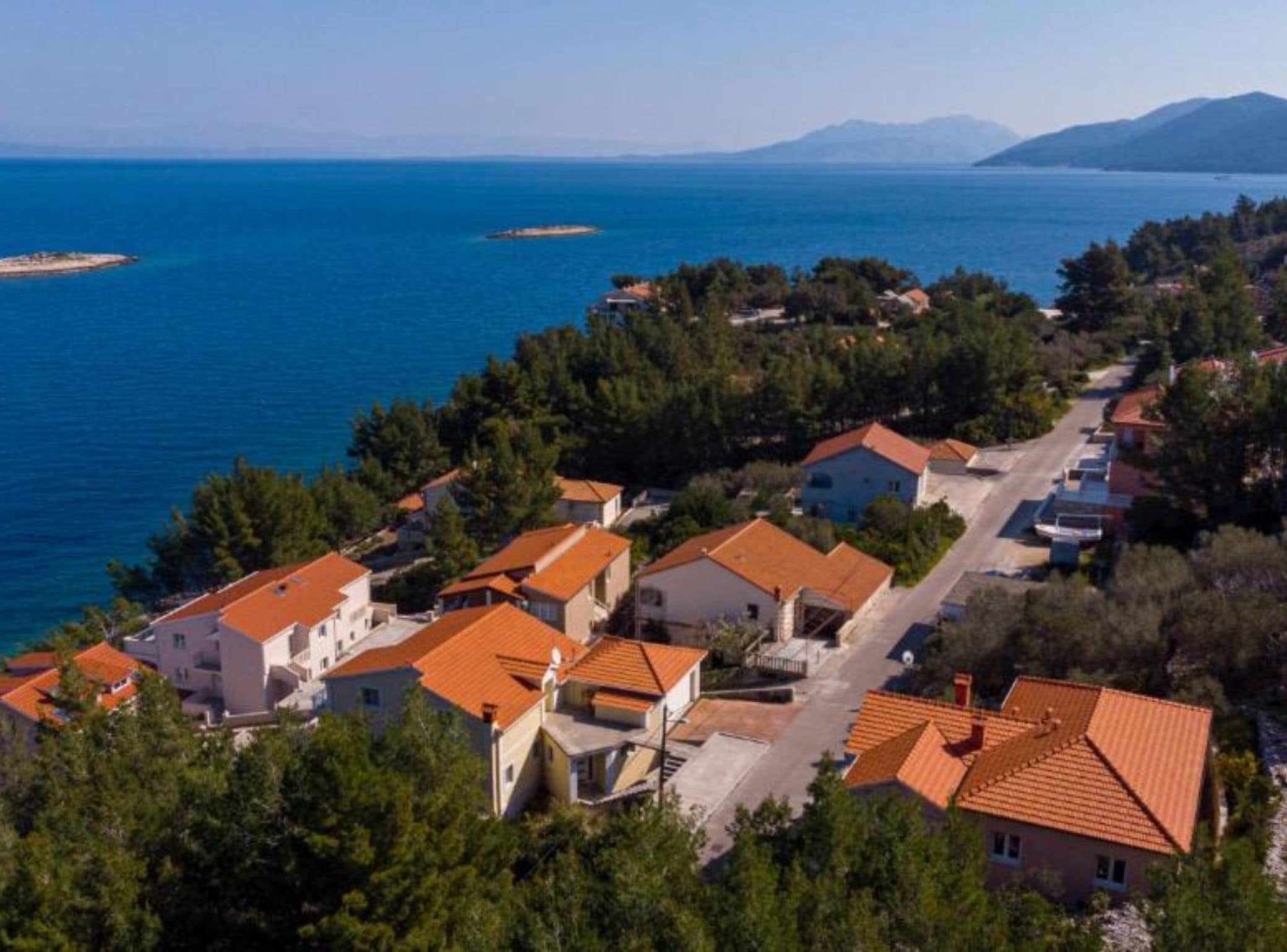 Un village côtier aux maisons aux toits de tuiles rouges, entouré de verdure et bordé par la mer.