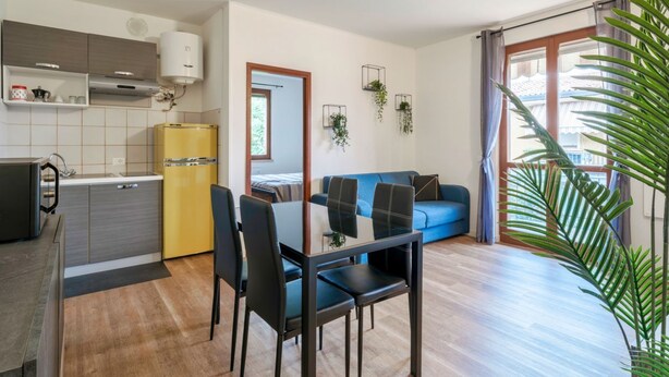 A compact living space with a kitchenette, a dining area, a sofa, and a large window with curtains. - Moretto 11. with pool and WiFi (Sirmione)